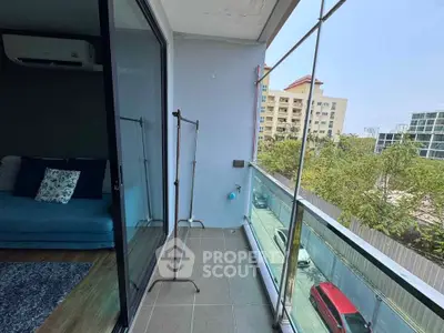 Modern balcony with glass railing and city view, adjacent to cozy living room with blue sofa.