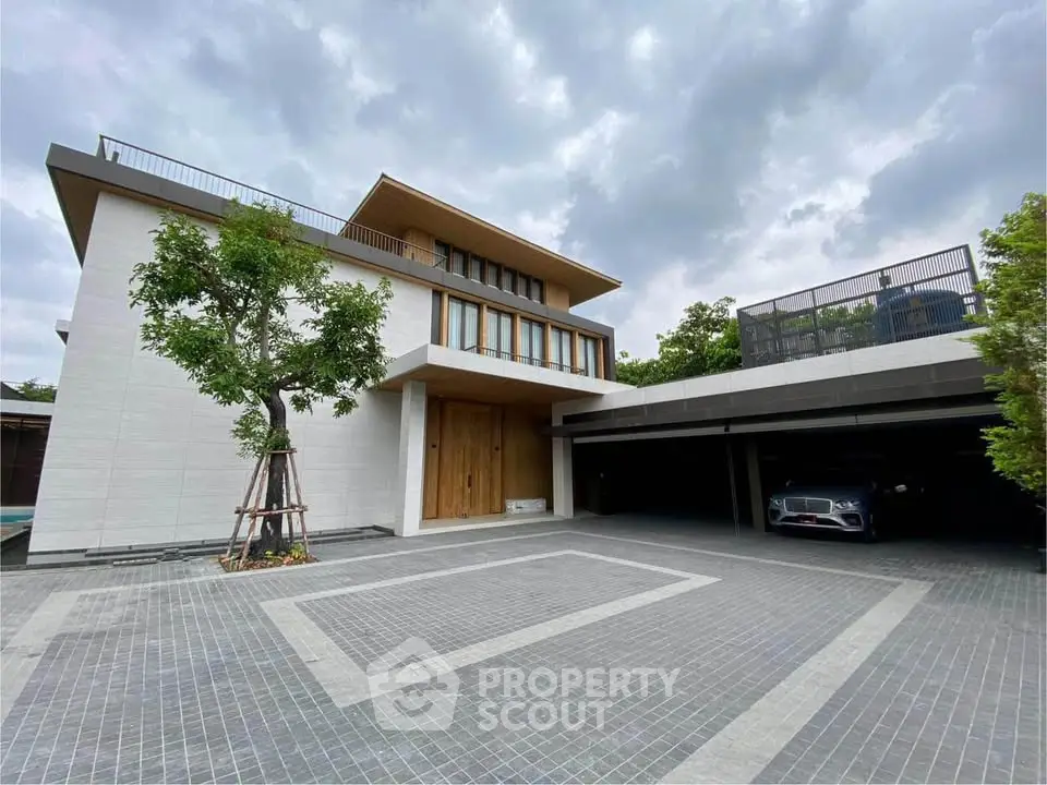 Luxurious modern house with spacious driveway and elegant architecture under a cloudy sky.
