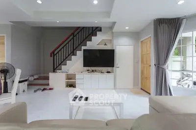 Modern living room with sleek staircase and wall-mounted TV, featuring neutral tones and natural light.