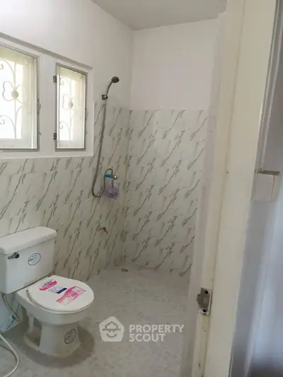 Compact bathroom with tiled walls and floor, featuring a toilet and shower area.