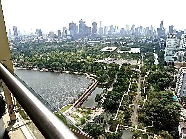 Stunning cityscape view from a high-rise balcony overlooking lush park and serene lake.