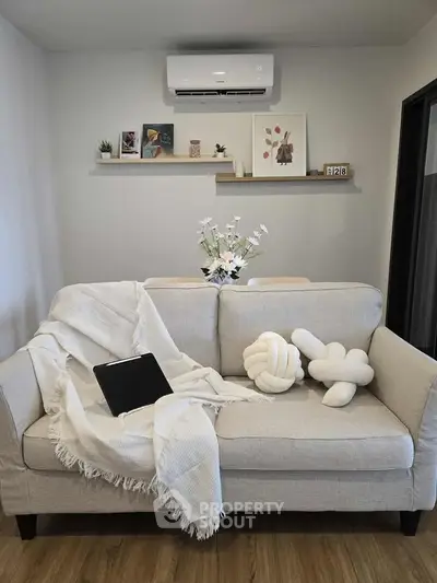 Cozy living room with modern decor, featuring a plush sofa, wall art, and air conditioning unit.