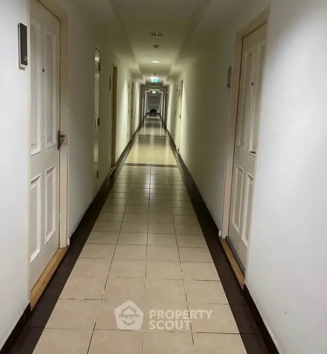 Spacious and well-lit corridor in a modern apartment building, featuring tiled flooring and multiple doors.