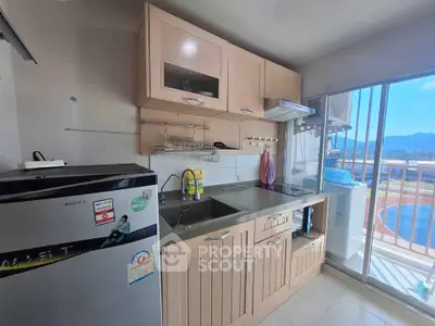 Modern kitchen with sleek cabinets and balcony view, featuring a compact fridge and stainless steel sink.