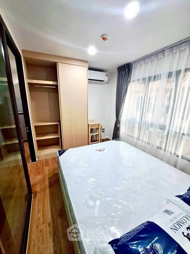 Modern bedroom with wooden flooring, large window, and built-in wardrobe in a bright apartment.