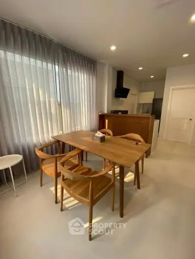 Modern dining area with wooden table and chairs, adjacent to a sleek kitchen.