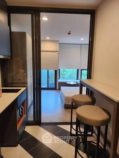 Modern studio apartment with open kitchen and cozy bedroom area, featuring stylish bar stools and natural light.