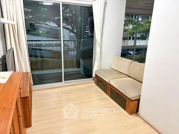 Cozy living room with wooden flooring and large windows overlooking greenery.