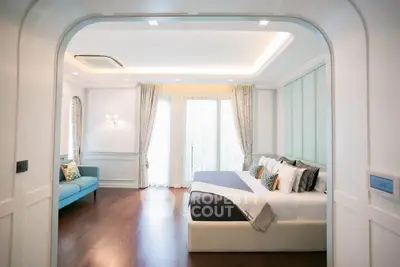 Luxurious bedroom with elegant decor and natural light, featuring a cozy seating area and stylish furnishings.