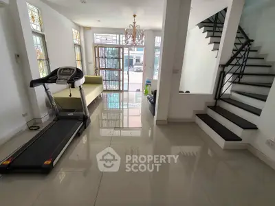 Spacious modern living room with treadmill and elegant staircase, featuring glossy tiled floors and large windows.