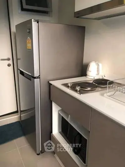 Modern kitchen with sleek appliances and compact design, featuring a fridge, stove, and microwave.