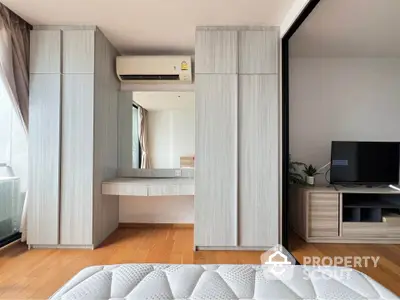 Modern bedroom with built-in wardrobe, air conditioning, and a cozy TV area, featuring sleek wooden flooring.