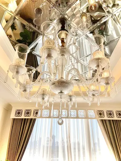 Luxurious chandelier in elegant living room with large windows and opulent curtains.