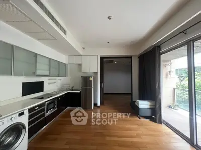 Spacious modern kitchen with open layout and balcony access, featuring sleek appliances and wooden flooring.