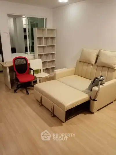 Modern living room with beige sofa bed and red office chair, perfect for relaxation and work.