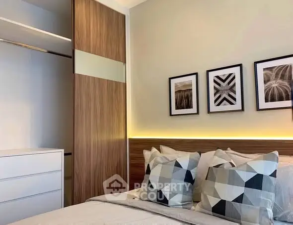 Modern bedroom with stylish decor and geometric pillows, featuring built-in wardrobe and framed art.
