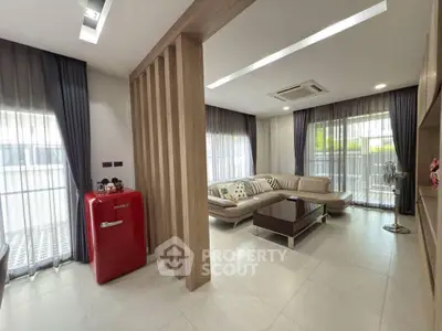 Modern living room with stylish decor and red mini fridge, featuring large windows and cozy seating area.