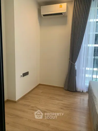 Modern bedroom with wooden flooring and air conditioning, featuring large window with elegant curtains.
