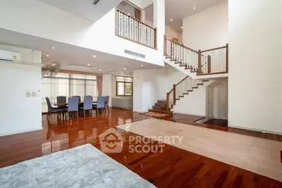 Spacious two-story living area with polished hardwood floors, elegant staircase, and ample natural light, perfect for luxurious living.