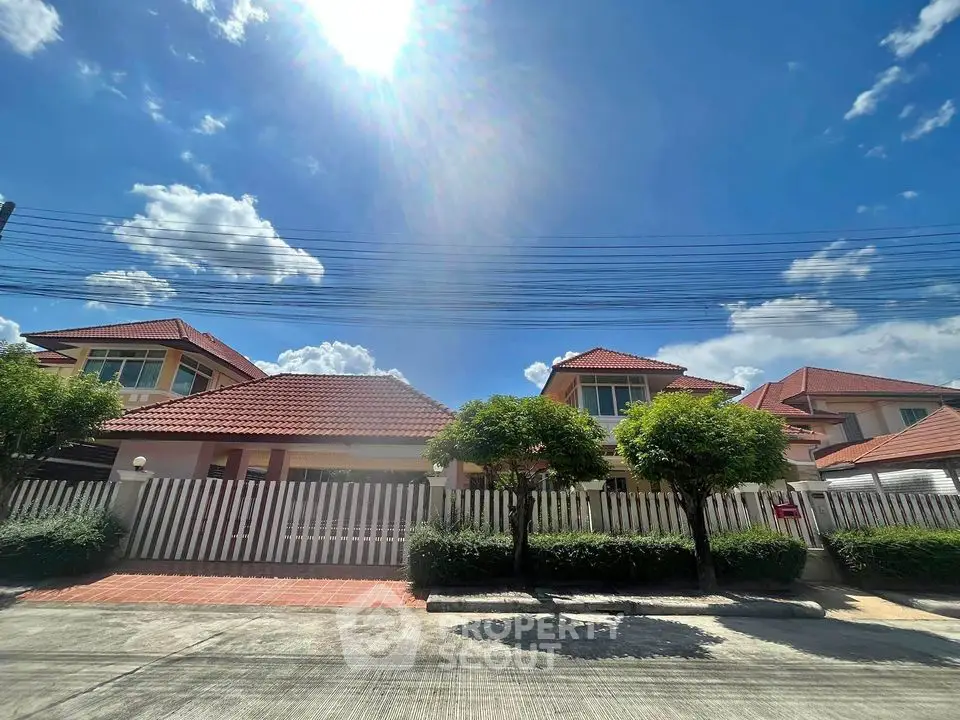 Charming suburban house with red roof and lush greenery under a clear blue sky.