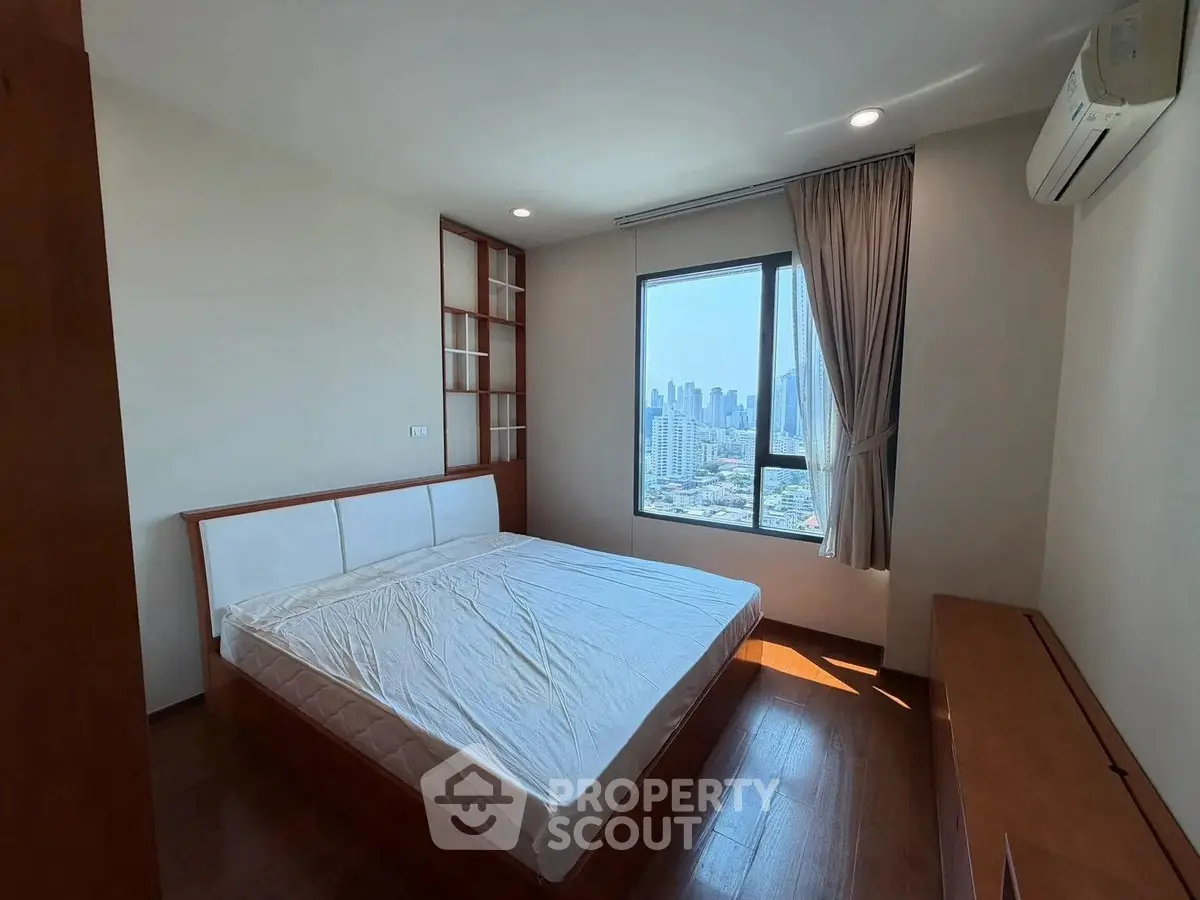 Spacious bedroom with city view, featuring wooden flooring and modern furnishings.