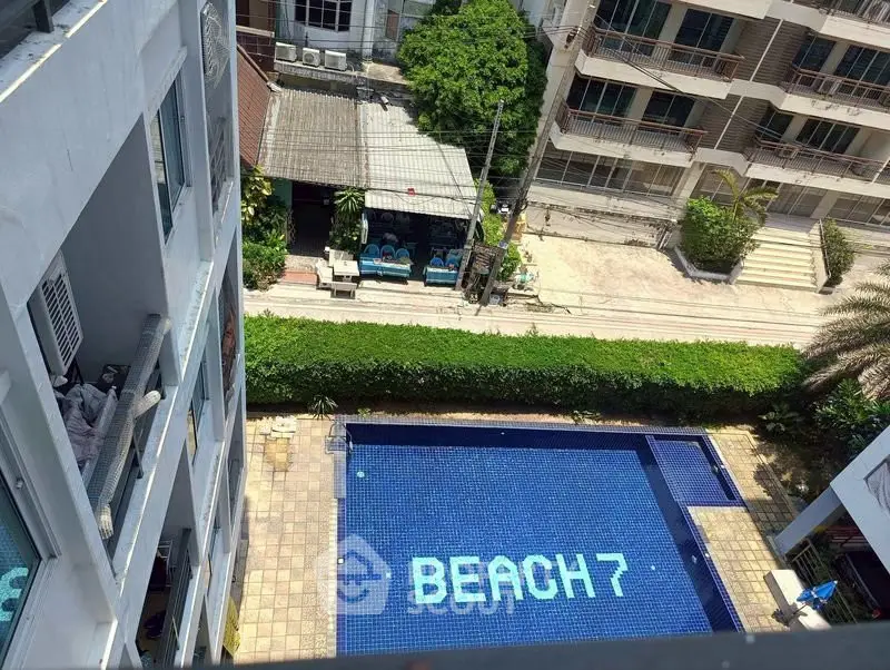 Stunning aerial view of a modern apartment complex with a sparkling pool and lush greenery, perfect for beach lovers.