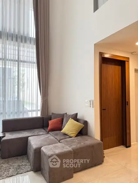 Modern living room with high ceilings and stylish furniture, featuring a cozy sectional sofa and elegant curtains.