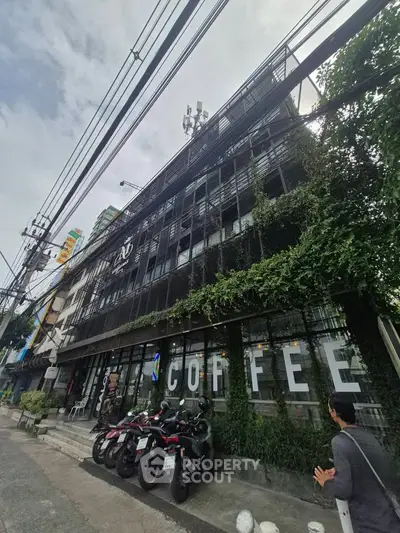 Chic urban building with lush greenery and street view, perfect for a trendy coffee shop location.