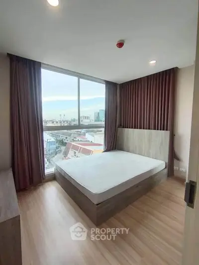 Modern bedroom with large window offering city view, featuring minimalist design and wooden flooring.