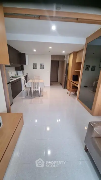 Modern open-layout living room with kitchen and dining area, featuring sleek furniture and bright lighting.