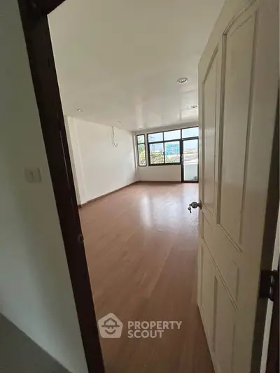 Spacious empty room with wooden flooring and large windows offering natural light.