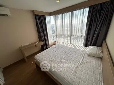 Modern bedroom with large windows offering stunning city views, featuring a cozy bed and elegant wooden flooring.