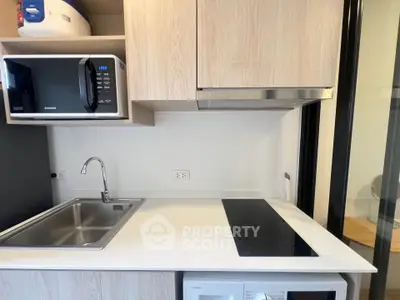 Modern kitchen with sleek appliances and minimalist design, featuring a built-in microwave and electric cooktop.