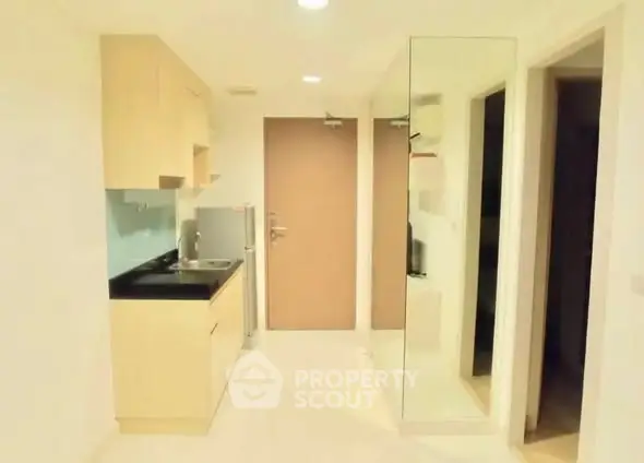 Compact modern kitchen with sleek cabinetry and mirrored wall in a cozy apartment.