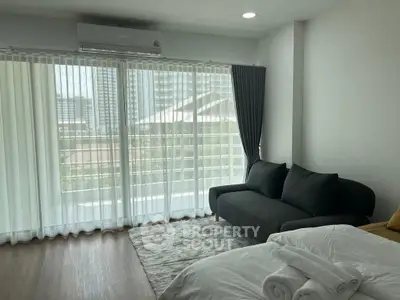 Modern bedroom with large windows and city view, featuring a cozy sofa and stylish decor.