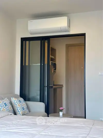 Modern studio apartment with air conditioning and sliding glass doors leading to a compact kitchen.