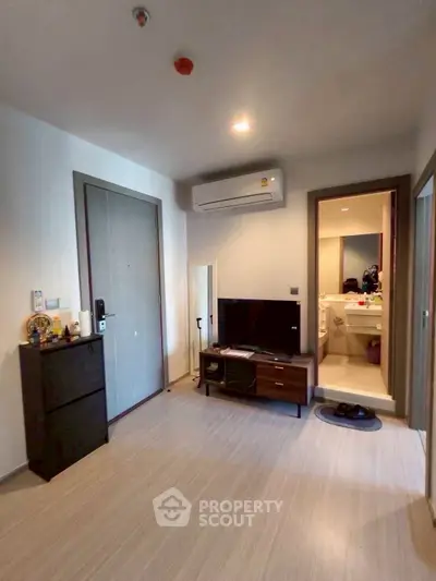 Modern living room with sleek furniture and air conditioning, leading to a compact bathroom.
