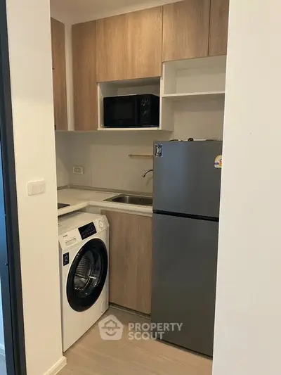 Compact modern kitchen with washing machine and fridge in a cozy apartment setting.