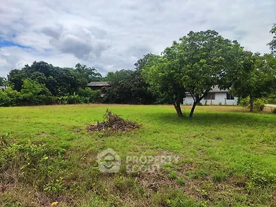 Expansive green land with trees and a distant house, perfect for development opportunities.