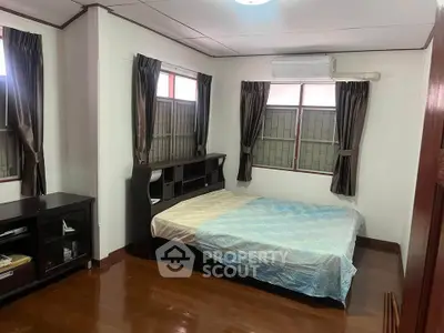 Cozy bedroom with wooden floors and natural light, featuring a comfortable bed and air conditioning.