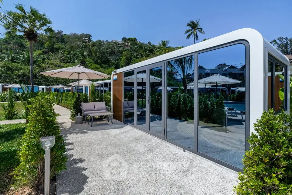 Modern poolside cabana with glass walls and lush greenery in a tropical resort setting.