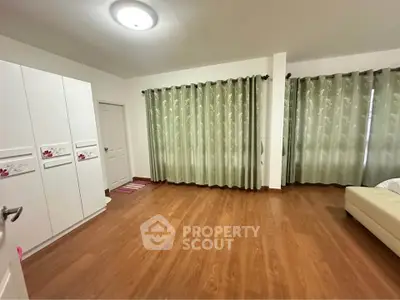 Spacious bedroom with wooden flooring and large windows for natural light.