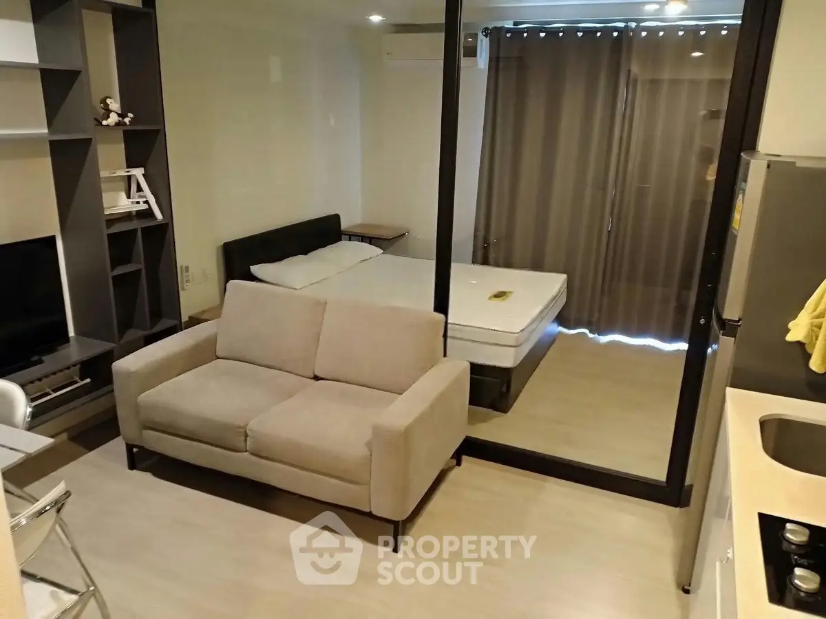 Modern studio apartment with cozy living area and bedroom separated by glass partition.