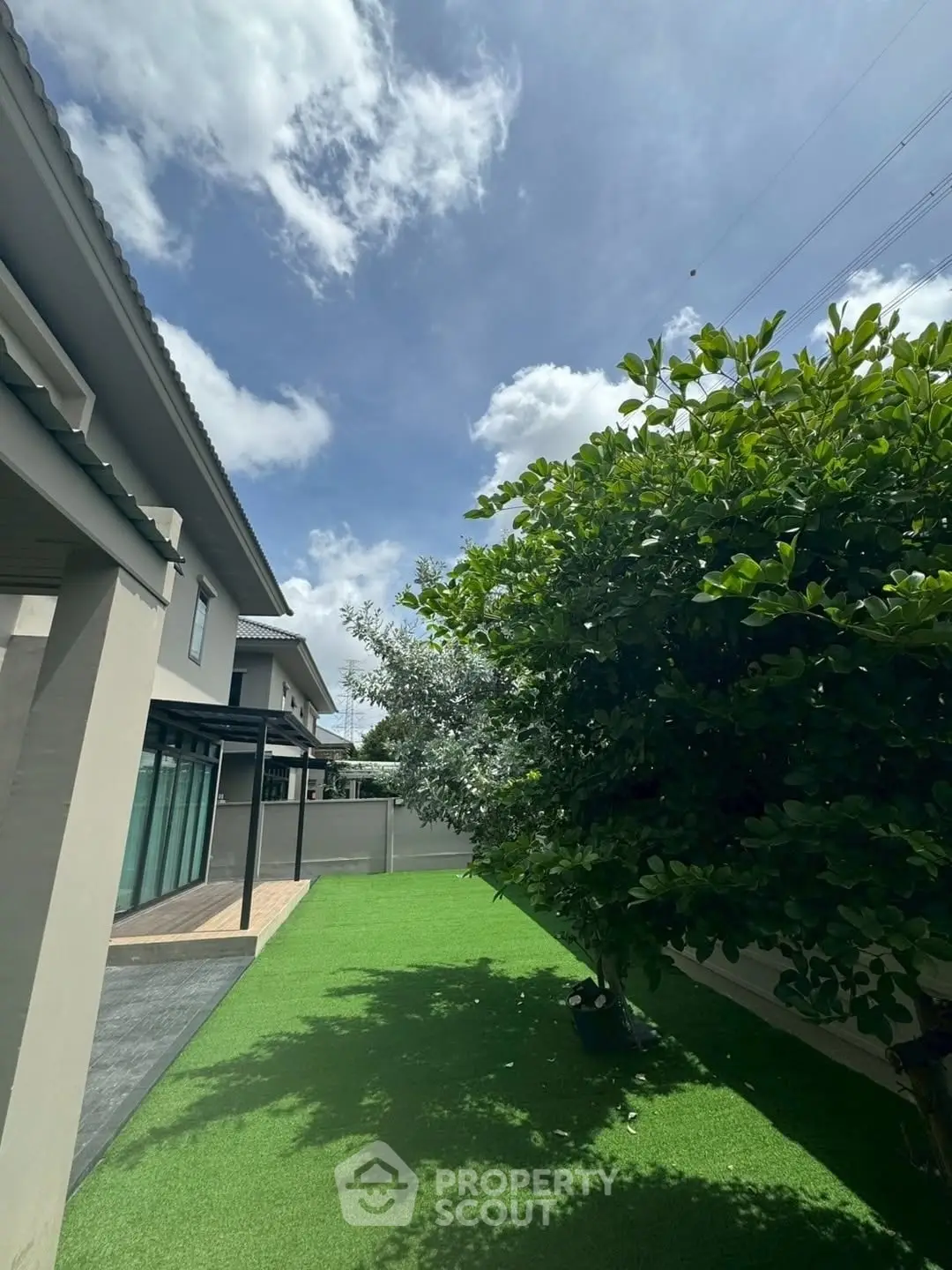 Spacious garden area with lush greenery and modern house exterior under a clear blue sky.