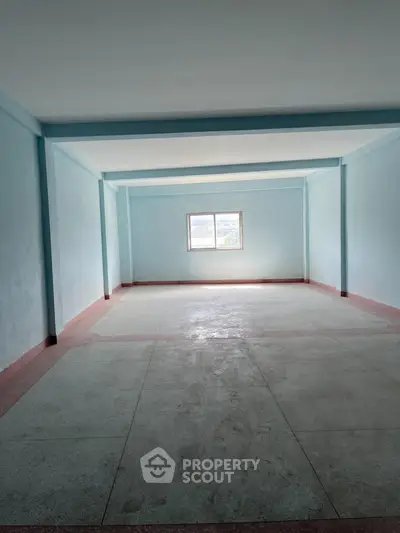 Spacious empty room with light blue walls and a single window, ideal for customization.