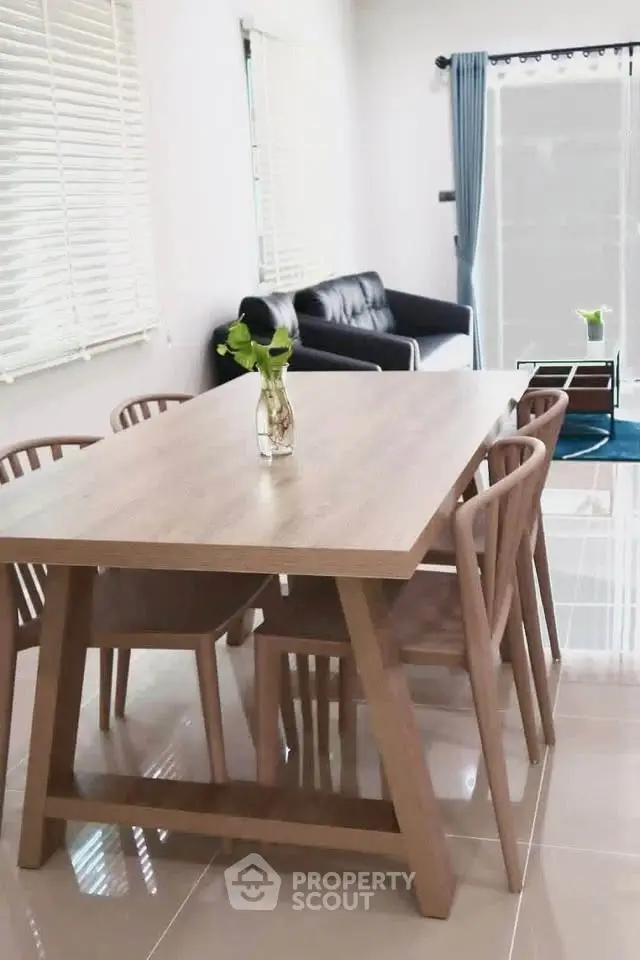 Modern dining area with wooden table and chairs, adjacent to cozy living room with sofa and glass table.