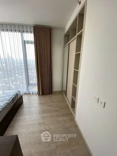 Modern bedroom with large window and built-in wardrobe offering city views.