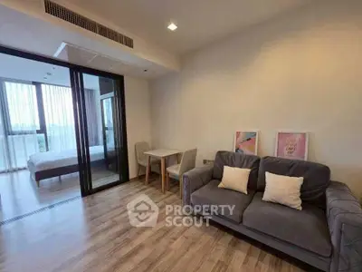 Modern living room with cozy sofa and dining area, adjacent to a bright bedroom with large windows.