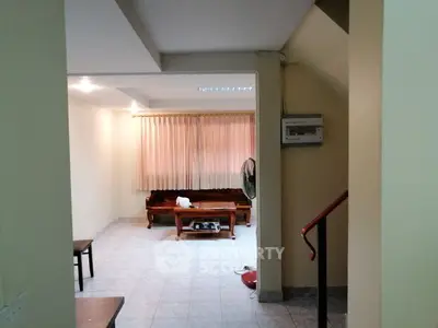 Cozy living room with tiled flooring and natural light, featuring simple furniture and a fan for comfort.