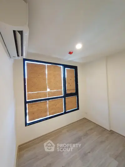 Bright empty room with wooden flooring and large window, perfect for customization.